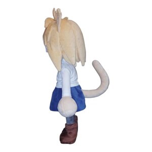 May include: A plush doll featuring a light blonde hair, white shirt, blue skirt, and brown boots. The doll has a long, curved tail and a round, white object attached to the front. The doll is facing away from the viewer.