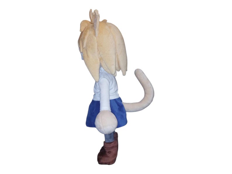 May include: A plush doll featuring a light blonde hair, white shirt, blue skirt, and brown boots. The doll has a long, curved tail and a round, white object attached to the front. The doll is facing away from the viewer.