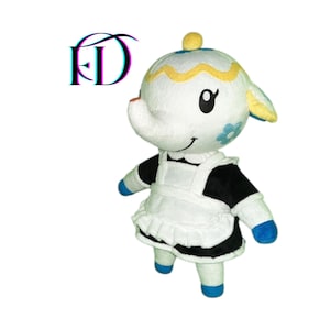 Puede incluir: Un peluche de un personaje de oveja blanca con un hocico grande, que lleva un atuendo de doncella en blanco y negro. La oveja tiene detalles azules y amarillos, una flor azul y una cara sonriente. El logotipo "FD" está en la esquina superior izquierda.