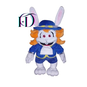 Peut inclure: Une peluche représentant un personnage avec un visage blanc, des yeux rouges et des cheveux roux. Le personnage porte une veste bleue, un short et un chapeau à bord jaune. Le jouet a des gants, des pieds et de longues oreilles de lapin blancs. Le logo "FD" est dans le coin supérieur gauche.