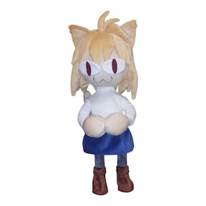 May include: A plush toy of a cat-like character with tan fur, large red eyes, and a white shirt. The character wears a blue skirt and brown boots. The toy has large, rounded paws and cat ears. The plush is standing upright.