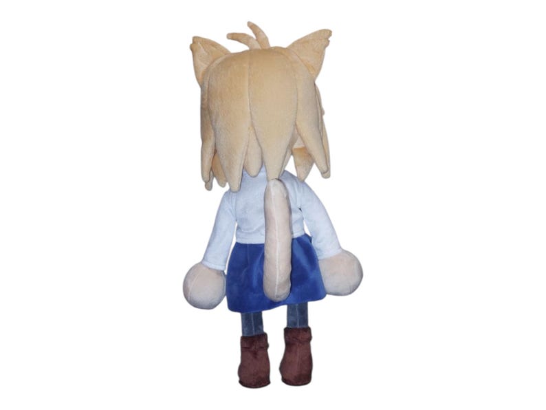 May include: A plush doll of a cat-like character, viewed from the back. It has tan fur, a white shirt, a blue skirt, and brown boots. The doll has large, round hands and a long tail.