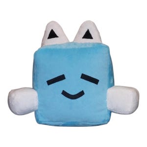 Puede incluir: Un peluche azul claro con forma de cubo con brazos y orejas blancos y redondeados. El juguete tiene una cara sonriente con ojos negros y una boca curva. Las orejas tienen acentos triangulares negros.