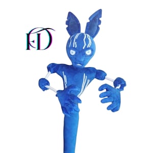 May include: A plush blue creature with large ears, white accents, and outstretched arms. The creature has a humanoid form with a long, cylindrical body and gloved hands. The image includes the letters "FD" in a stylized font.