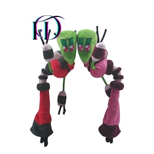 May include: Two plush toys with green, oblong heads and pink and white details. The toys have segmented bodies in black, white, red, and pink. The toys have long, dangling appendages in red and pink with black tips. The toys are set against a white background.