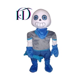 Puede incluir: Un peluche de un personaje con una cabeza blanca con forma de calavera, ojos azules y una amplia sonrisa. El personaje lleva una camisa gris, una bufanda azul, guantes y pantalones. El texto "FD" está en la esquina superior izquierda.