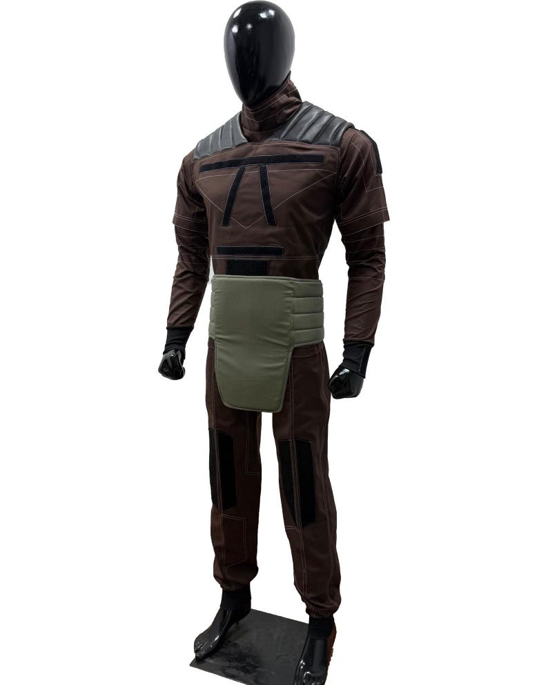 May include: A brown and black costume displayed on a mannequin. The costume features a high collar, shoulder pads, and a green waist belt. The pants have black patches on the knees. The mannequin has a black head and hands.