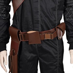 May include: A brown leather gun belt with a holster, pouches, and a cartridge holder. The belt is worn over a black jumpsuit. The belt has a rectangular buckle and is designed for a costume or cosplay.