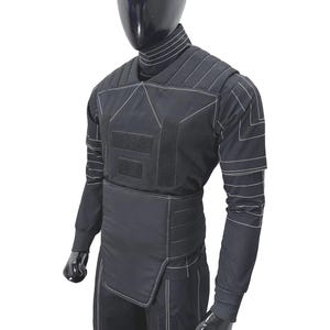 May include: Black protective suit with white stitching, shown on a mannequin. The suit comprises a long-sleeved top, trousers, and a vest-like element with hook-and-loop fastenings. The design incorporates geometric patterns and reinforced sections.