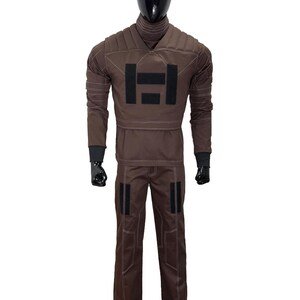 May include: A brown costume displayed on a black mannequin. The outfit includes a long-sleeved top with a black emblem and matching pants. The costume has black accents and white stitching.