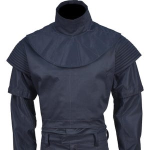 May include: A navy blue garment with a high collar and structured shoulders. The design features a layered construction with pleated details on the shoulders and a fitted waist. The sleeves are long, and the overall style is utilitarian.