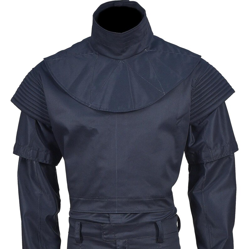May include: A navy blue garment with a high collar and structured shoulders. The design features a layered construction with pleated details on the shoulders and a fitted waist. The sleeves are long, and the overall style is utilitarian.