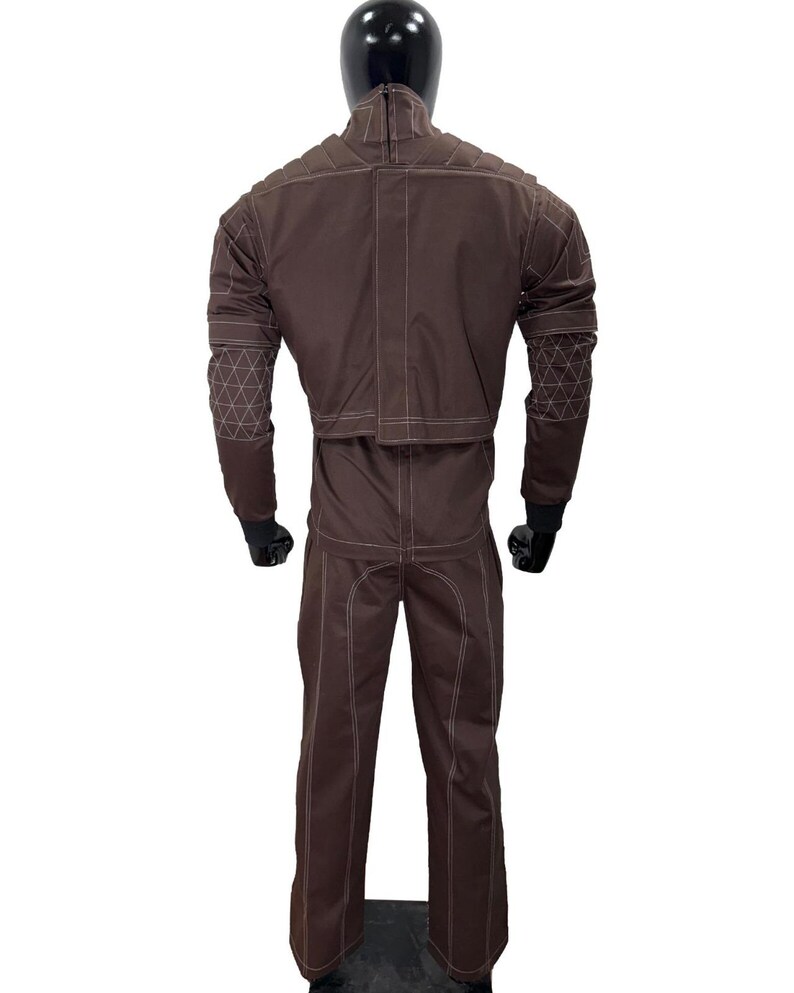 May include: A brown jumpsuit with white stitching and geometric patterns on the sleeves. The suit is displayed on a mannequin, showcasing its design and construction. The jumpsuit has a high collar and a zipper closure.