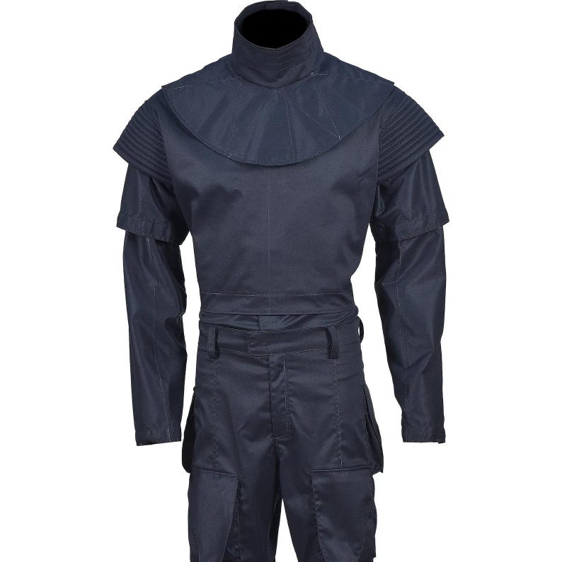 May include: A dark navy blue jumpsuit with a high collar and layered shoulder details. The long-sleeved garment features a cinched waist and multiple pockets on the pants. The overall design suggests a futuristic or military-inspired aesthetic.