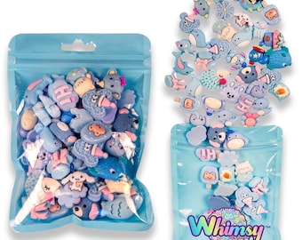 Puede incluir: Dos bolsas de plástico transparente llenas de abalorios azules y de colores pastel surtidos. Los abalorios presentan varias formas, incluyendo animales, alimentos y otros diseños caprichosos. La bolsa de la derecha tiene la palabra "Whimsy" impresa.