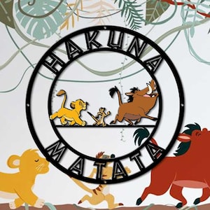 May include: A circular black metal wall sign featuring the text HAKUNA MATATA in bold capital letters. Inside the circle, a silhouette depicts a small lion cub, a meerkat, and a warthog walking in a line on a horizontal bar across the center.