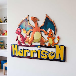 May include: A wall-mounted wooden sign featuring the name Harrison in yellow letters with a blue outline. Above the name are three colorful cartoon dragon-like creatures, including a large orange one with wings and two smaller red and orange ones.