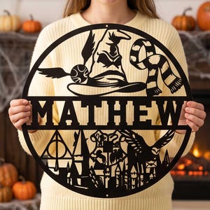 May include: A circular black metal wall sign featuring the name MATHEW in bold capital letters. The design includes a wizard hat, a winged ball, a striped scarf, a castle silhouette, a crest, and a flying owl within the circular frame.
