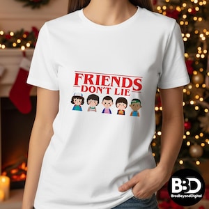 May include: White t-shirt featuring the text "FRIENDS DON'T LIE" in red, above a graphic of five cartoon characters. The characters are in various outfits and hairstyles. The shirt is a crew neck.