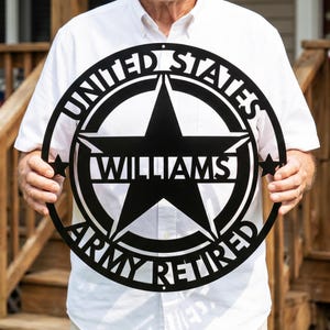 May include: Black metal sign with the text "UNITED STATES ARMY RETIRED" encircling a star with the name "WILLIAMS" in the center. The sign is held up by a person.