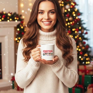 May include: White ceramic mug with the text "FRIENDS DON'T LIE" in red and a graphic of cartoon characters. The mug is held in front of a Christmas tree and fireplace.