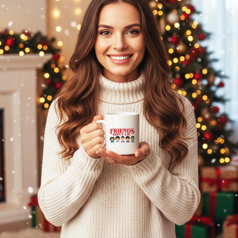 May include: White ceramic mug with the text "FRIENDS DON'T LIE" in red and a graphic of cartoon characters. The mug is held in front of a Christmas tree and fireplace.