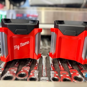 May include: Two red and black tool organizers with the text "My Name" in white. The organizers have a rectangular shape with gray accents and are sitting on top of a set of wrenches.