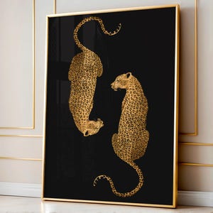 May include: A framed art print showing two golden leopard illustrations against a black backdrop. The leopards are detailed with spots, one upside down, the other upright. The frame has a gold finish, adding a touch of elegance to the artwork.