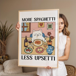 Könnte beinhalten: Gerahmter Kunstdruck mit einer Cartoon-Katze, die Spaghetti isst. Der Druck enthält den Text "MORE SPAGHETTI LESS UPSETTI" in einer verspielten Schriftart. Das Kunstwerk hat einen Retro-Stil mit einer Farbpalette aus Rosa, Beige und Blau.