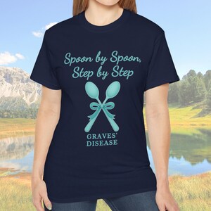 Puede incluir: Camiseta azul marino con el texto "Spoon by Spoon, Step by Step" sobre una ilustración turquesa de cucharas cruzadas atadas con un lazo. El texto "GRAVES' DISEASE" está debajo. La camiseta es de cuello redondo.