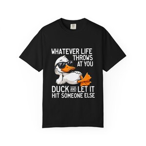 Op de afbeelding: Een zwart t-shirt met korte mouwen en een afbeelding van een witte eend met een zwarte zonnebril, liggend met het hoofd op de vleugel. De tekst luidt: WHATEVER LIFE THROWS AT YOU DUCK AND LET IT HIT SOMEONE ELSE in witte hoofdletters.