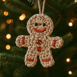Könnte beinhalten: Handgefertigter, beige gehäkelter Lebkuchenmann-Weihnachtsschmuck. Der Schmuck hat einen roten, lächelnden Mund, schwarze Augen und rote Edelstein-Knöpfe. Roter Faden akzentuiert die Arme und Beine. Er hängt an einer beigen Garnschlaufe.