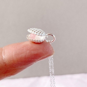 Op de afbeelding: Zilveren hangerketting met een schelpontwerp. De schelp opent en onthult een roze parel. De hanger hangt aan een fijne zilveren ketting, waardoor een elegant sieraad ontstaat.