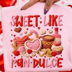 May include: A pink tote bag with the words "SWEET LIKE PAN DULCE" in red and pink embroidered letters. The bag features embroidered images of cookies, hearts, a coffee cup, and a bottle. Red heart-shaped balloons are in the background.