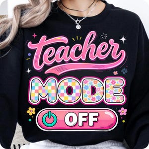 May include: Black sweatshirt with the words "Teacher Mode Off" in a colorful design. The text "Teacher" is in pink script, and "Mode" is in a checkered pattern. The word "Off" is in a pink button design.