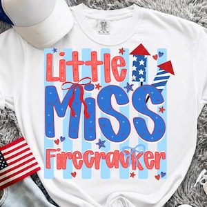 Peut inclure: Un t-shirt blanc avec une impression graphique portant le texte Little Miss Firecracker en rouge et bleu. Le motif comprend des feux d'artifice, des étoiles, des cœurs et des nœuds rouges et bleus sur des rayures verticales bleu clair.