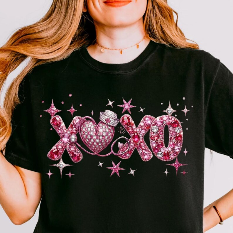 May include: Black t-shirt with a pink rhinestone design featuring the letters "XOXO", a heart, and a nurse's hat. The design is embellished with stars and sparkles. The shirt is a crew neck.