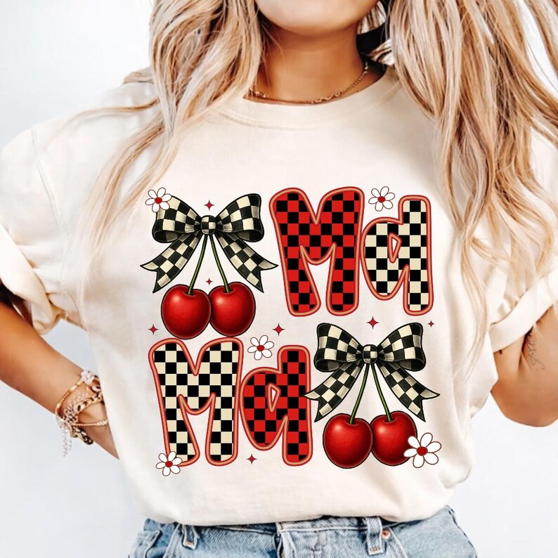 May include: Cream-colored t-shirt featuring the text "Md Md" in a checkerboard pattern with red accents. The design includes cherries and black and white checkered bows, with small white flowers scattered around the text.