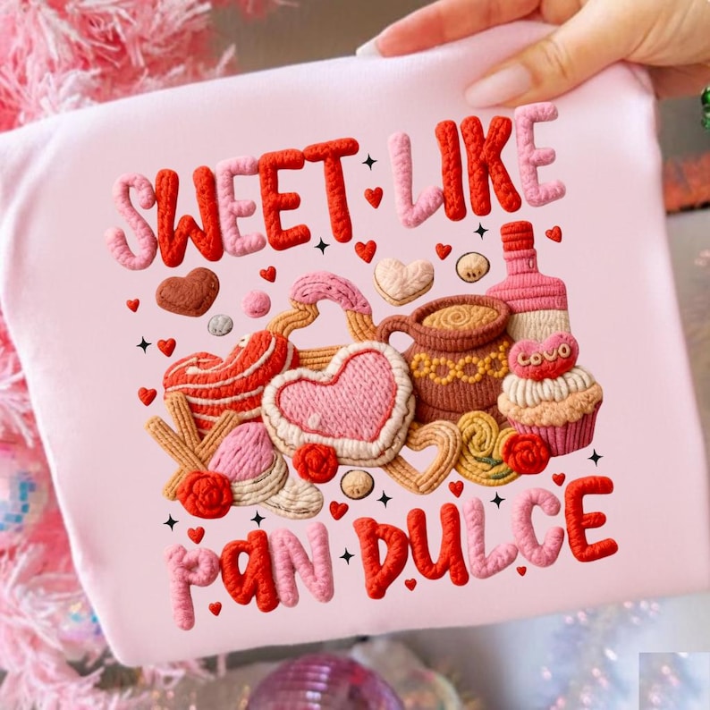May include: A light pink t-shirt with the words "SWEET LIKE PAN DULCE" in red and pink textured lettering. The shirt features a colorful illustration of various baked goods, including cookies, a cupcake, and a bottle.