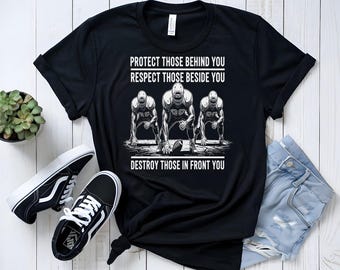 May include: Black t-shirt with the text "PROTECT THOSE BEHIND YOU RESPECT THOSE BESIDE YOU DESTROY THOSE IN FRONT YOU" and a graphic of three football players. Black and white sneakers and a small potted plant are also in the image.