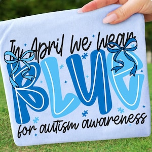 May include: Light blue fabric with the text "In April we wear BLUE for autism awareness" in a mix of fonts and shades of blue. The word "BLUE" is the largest element, with a bow graphic.