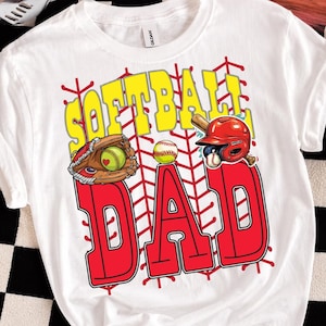 Op de afbeelding: Wit t-shirt met een softbalthema. Het ontwerp toont de woorden "SOFTBALL DAD" in geel en rood, samen met een softbal, handschoen en helm afbeelding. Het shirt is gemaakt van een zacht materiaal.