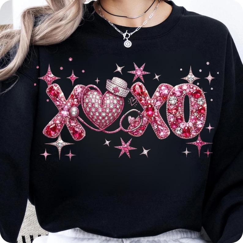 May include: Black sweatshirt with a pink and red rhinestone design. The design features the letters "XOXO" with a heart, stars, and a nurse's hat. The letters and heart are embellished with rhinestones, creating a sparkling effect.