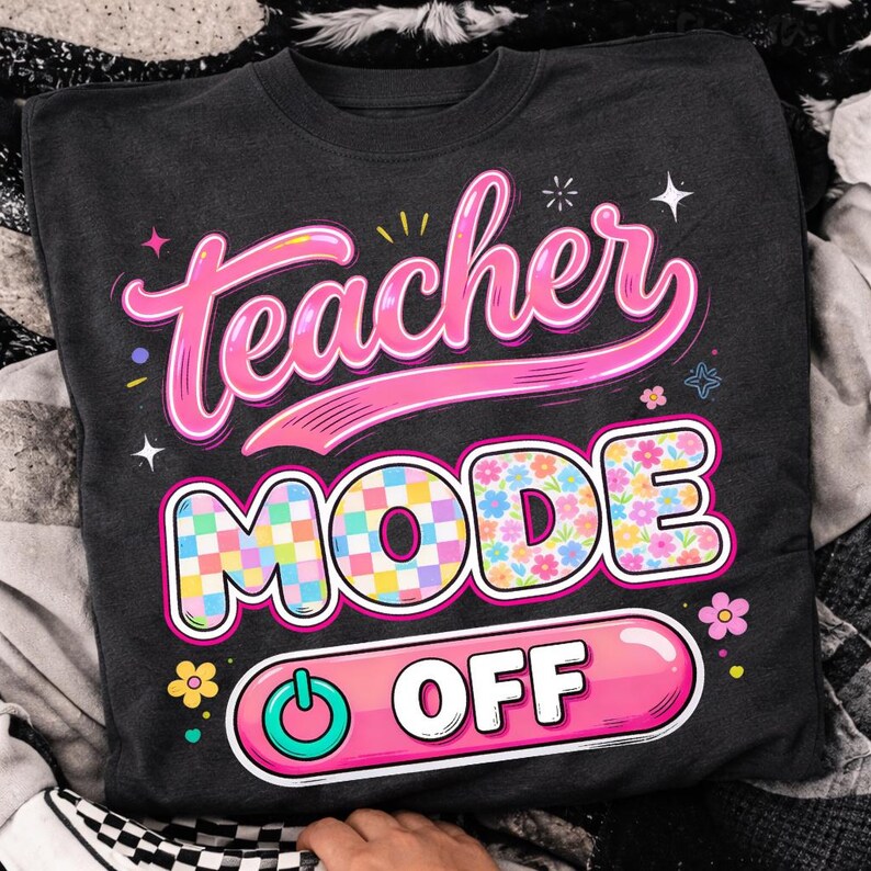 May include: Dark gray t-shirt with the words "Teacher Mode Off" in pink and white. The word "Teacher" is in a cursive font, and "Mode" is in a checkered pattern. The word "Off" is in a pink button.