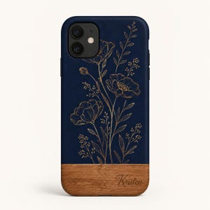 Könnte beinhalten: Eine marineblaue Smartphone-Hülle mit einer goldfarbenen Linienzeichnung von Wildblumen und Stängeln. Der untere Teil der Hülle besteht aus hellbraunem Holz, in das der Name Kristen in einer kursiven Schreibschrift unten rechts eingraviert ist.