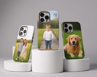 Op de afbeelding: Drie gepersonaliseerde smartphonehoesjes met fotoprints. Het linkerhoesje toont twee personen in een veld, het middelste hoesje een kind op een houten pad en het rechterhoesje een golden retriever die in het groene gras ligt.