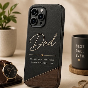 Könnte beinhalten: Schwarze Handyhülle mit dem Wort "Dad" in goldener Schrift. Die Hülle hat einen Holzmaserungsboden und den Text "THANKS FOR EVERYTHING OLIVIA • MASON • AVA". Eine Uhr, ein Becher und ein Anhänger mit der Aufschrift "MADE FOR DAD" sind ebenfalls zu sehen.