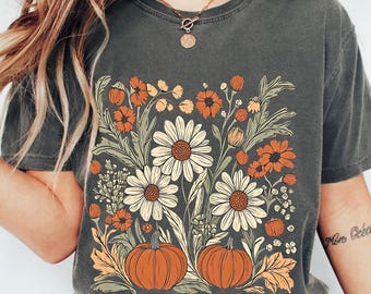 May include: Dark gray t-shirt featuring a floral design with daisies, orange flowers, and pumpkins. The design has a vintage, fall-themed aesthetic. The shirt is a comfortable, casual style.