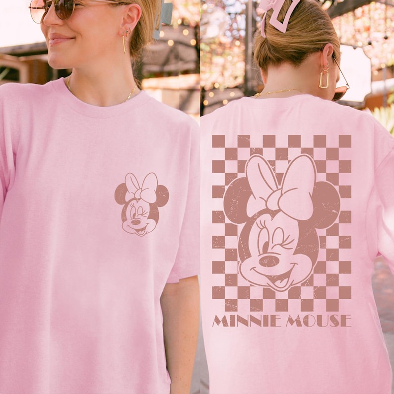 Puede incluir: Camiseta rosa claro con un dise&ntilde;o de Minnie Mouse. La parte delantera tiene un peque&ntilde;o dise&ntilde;o de Minnie Mouse, mientras que la parte trasera muestra una imagen m&aacute;s grande de Minnie Mouse sobre un fondo a cuadros marr&oacute;n y blanco, con las palabras "MINNIE MOUSE" debajo.