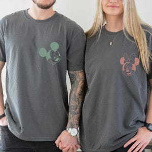 Puede incluir: Dos camisetas gris carb&oacute;n, cada una con un dise&ntilde;o de personaje de Disney. Una camiseta tiene un dise&ntilde;o de Mickey Mouse verde, y la otra un dise&ntilde;o de Minnie Mouse rosa. Ambas camisetas son de manga corta y de corte holgado.